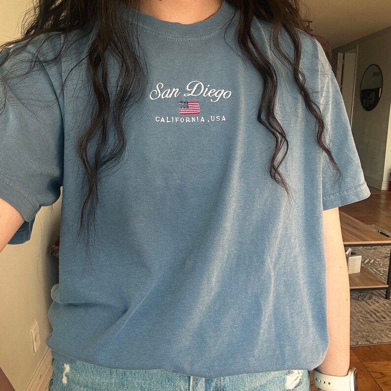 May include: A light blue t-shirt with the text "San Diego, California, USA" and a small American flag embroidered on the front.