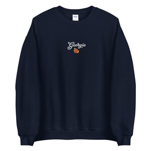 K&ouml;nnte beinhalten: Marineblauer Sweatshirt mit einer wei&szlig;en gestickten Pfirsich und dem Text "Georgia" auf der Vorderseite.