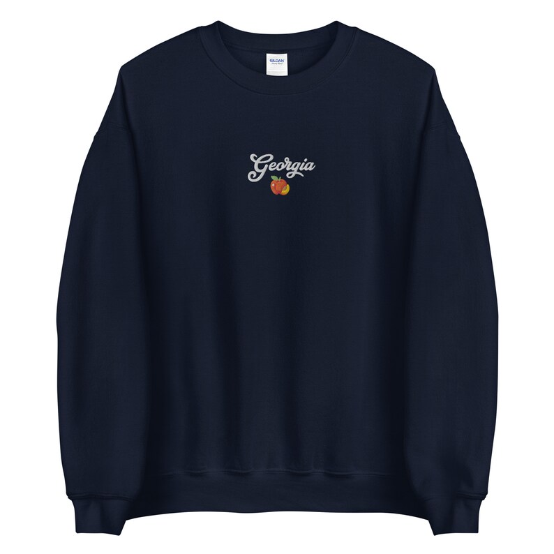K&ouml;nnte beinhalten: Marineblauer Sweatshirt mit einer wei&szlig;en gestickten Pfirsich und dem Text "Georgia" auf der Vorderseite.