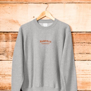 May include: A gray sweatshirt with a brown embroidered logo that says "NASHVILLE TENNESSEE".