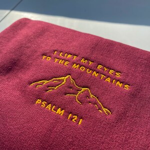 May include: Burgundy sweatshirt with yellow embroidered text that reads "I lift my eyes to the mountains Psalm 121".