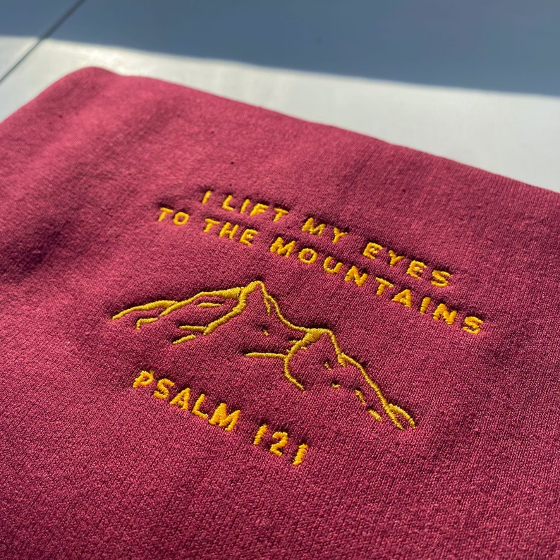 May include: Burgundy sweatshirt with yellow embroidered text that reads "I lift my eyes to the mountains Psalm 121".