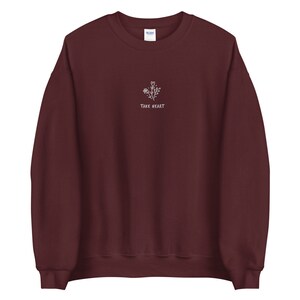 May include: Burgundy sweatshirt with a white embroidered design of a flower with the text "Take Heart".