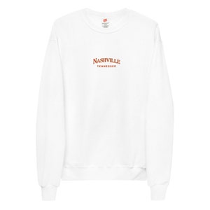 May include: White long-sleeve sweatshirt with a brown embroidered design that says "NASHVILLE TENNESSEE".