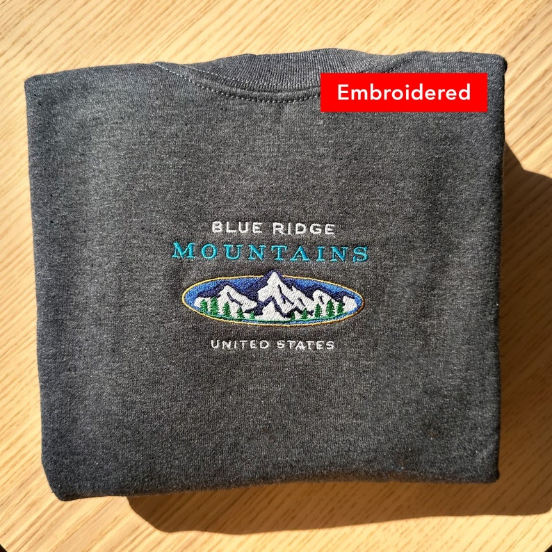 Op de afbeelding: Een donkergrijs sweatshirt met een geborduurd logo met de tekst "Blue Ridge Mountains United States".