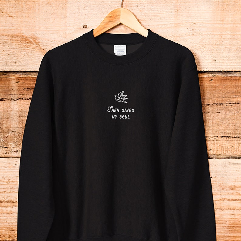 Puede incluir: Sudadera negra con un p&aacute;jaro bordado en blanco y el texto "Then Sings My Soul".