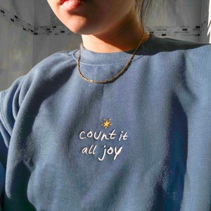 May include: A blue sweatshirt with the text "count it all joy" embroidered in white with a small gold star above the text.