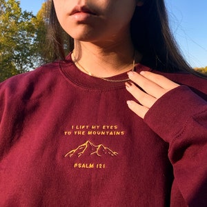 May include: Burgundy sweatshirt with a gold embroidered mountain design and the text "I lift my eyes to the mountains Psalm 121".