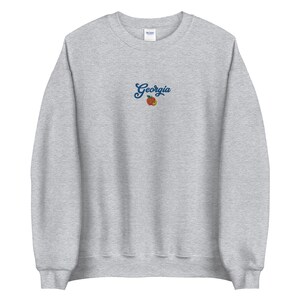 K&ouml;nnte beinhalten: Grauer Sweatshirt mit einem Pfirsich und dem Wort "Georgia" auf der Vorderseite gestickt.