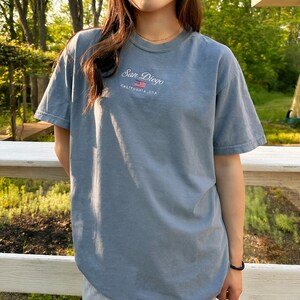 May include: A light blue t-shirt with a white embroidered design that says "San Diego, California, USA" with a small American flag graphic.