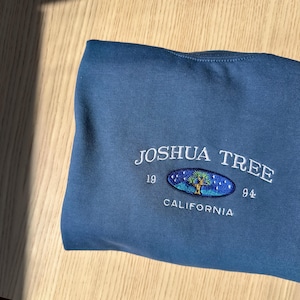 May include: A blue sweatshirt with a white embroidered logo that says "Joshua Tree 1994 California" with a stylized tree inside an oval.