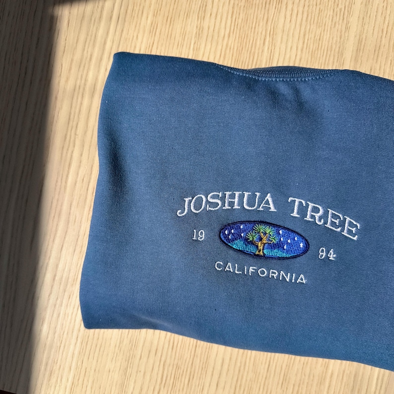 May include: A blue sweatshirt with a white embroidered logo that says "Joshua Tree 1994 California" with a stylized tree inside an oval.
