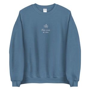 Puede incluir: Una sudadera azul con un p&aacute;jaro bordado en blanco y el texto "Then Sings My Soul".