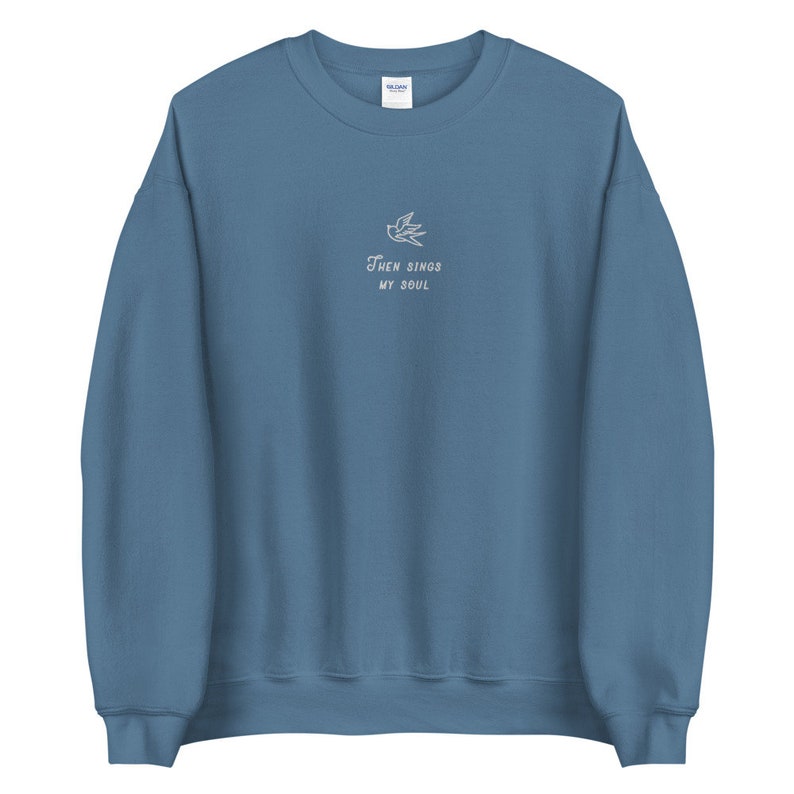 Puede incluir: Una sudadera azul con un p&aacute;jaro bordado en blanco y el texto "Then Sings My Soul".