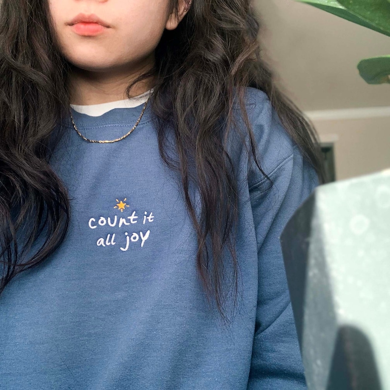 May include: A blue sweatshirt with the text "count it all joy" embroidered in white with a small yellow star above the word "count".