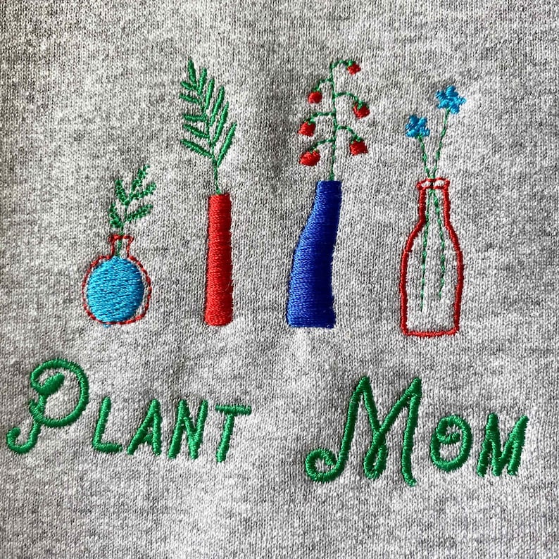 May include: Embroidered gray sweatshirt with the text "Plant Mom" in green thread. The design features four embroidered vases with different colored flowers and plants.