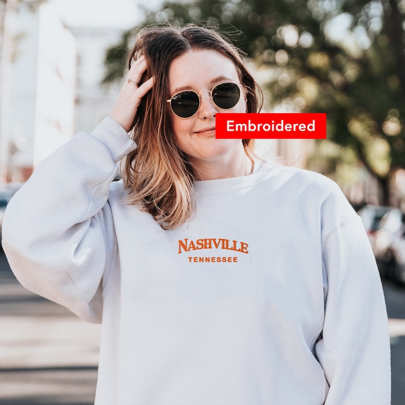 May include: White sweatshirt with an orange embroidered design that says "Nashville Tennessee".