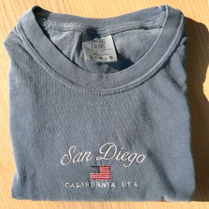 May include: A light blue t-shirt with the text "San Diego, California, USA" and a small embroidered American flag.