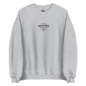 May include: A heather grey sweatshirt with a small embroidered logo on the front. The logo says "Wyoming Bighorn National Forest" with a stylised flower design.