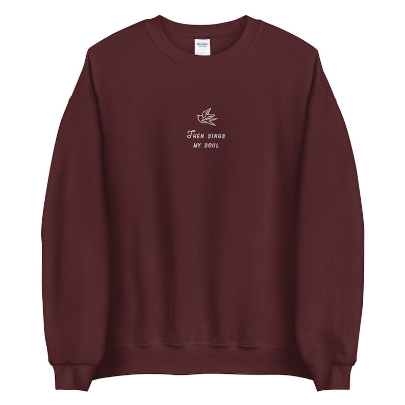 Puede incluir: Una sudadera color granate con un dise&ntilde;o bordado en blanco de un p&aacute;jaro y el texto "Then Sings My Soul".