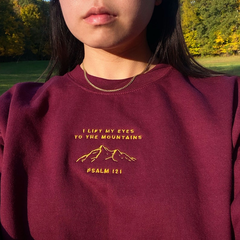 May include: A maroon sweatshirt with a gold embroidered design that reads "I lift my eyes to the mountains Psalm 121".