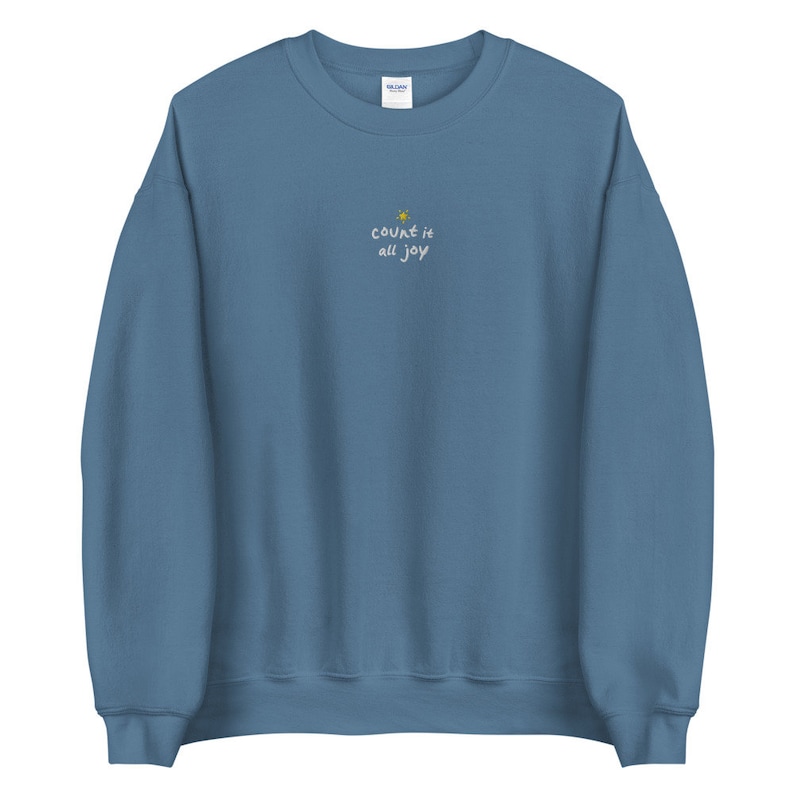 May include: A blue sweatshirt with the text "count it all joy" embroidered on the front. A small yellow star is above the text.