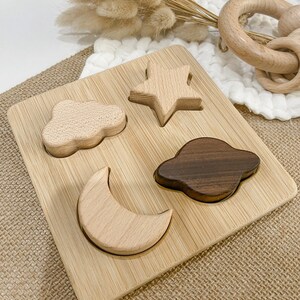 May include: A wooden puzzle with four shapes: a star, a cloud, a crescent moon, and a planet. The puzzle pieces are made of light and dark wood and fit into corresponding cutouts on a bamboo board.