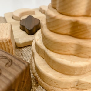 May include: A wooden stacking toy with a flower-shaped design. The toy is made of natural wood and has a light brown color. The toy is on a burlap surface.