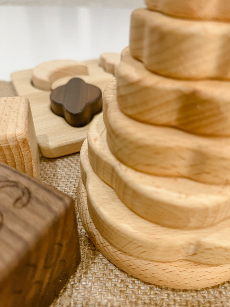 May include: A wooden stacking toy with a flower-shaped design. The toy is made of natural wood and has a light brown color. The toy is on a burlap surface.
