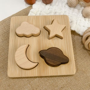 May include: A wooden puzzle board with four shapes: a cloud, a star, a crescent moon, and a planet. The shapes are made of different types of wood, and the board is made of bamboo.