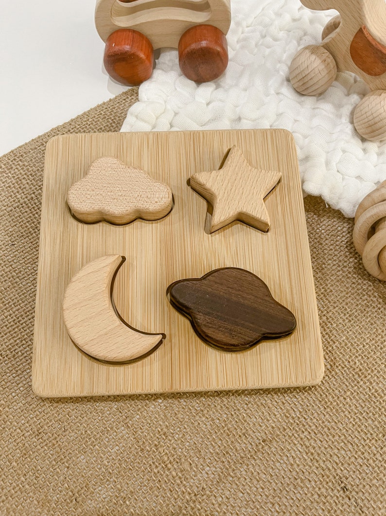 May include: A wooden puzzle board with four shapes: a cloud, a star, a crescent moon, and a planet. The shapes are made of different types of wood, and the board is made of bamboo.