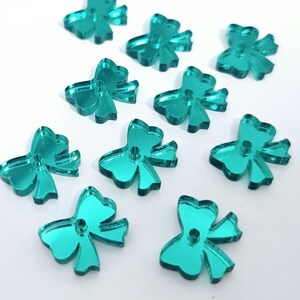 May include: Ten teal blue mirrored bow-shaped buttons. The buttons are made of acrylic and have a shiny finish.