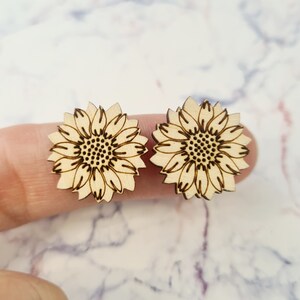 May include: A pair of wooden sunflower earrings. The earrings are laser cut and have a natural wood finish.