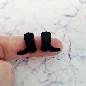 May include: A pair of black cowboy boot earrings. The boots are made of a smooth, matt material and have a classic western style.
