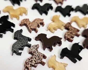 May include: A selection of miniature horse-shaped decorations in diverse colours and finishes. The collection features black, brown, gold, and glittery pieces, ideal for crafting and creative projects.