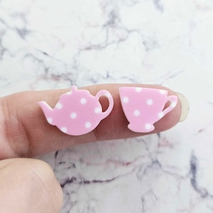 May include: A pair of pink and white polka dot earrings shaped like a teapot and a teacup.