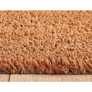 May include: A brown coir doormat with a textured surface. The doormat is made of natural fibers and has a rubber backing.