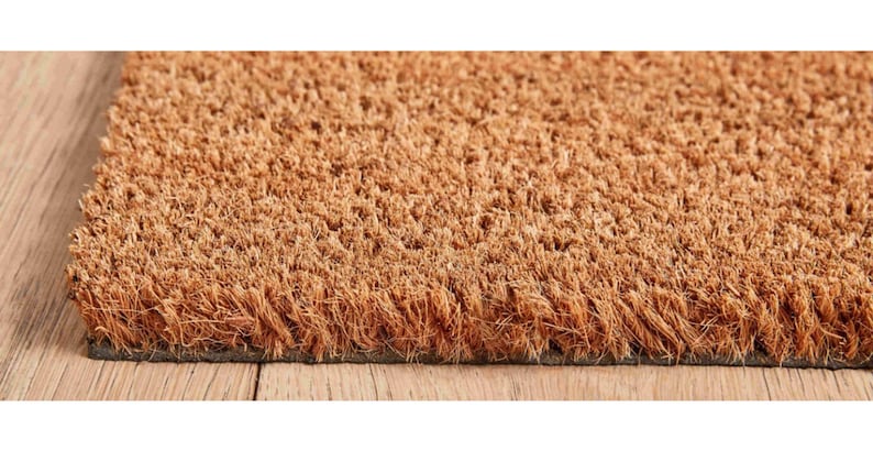 May include: A brown coir doormat with a textured surface. The doormat is made of natural fibers and has a rubber backing.