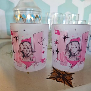 May include: Two frosted glass tumblers with a pink and white geometric design featuring a woman's portrait and the text "Stars" in black.
