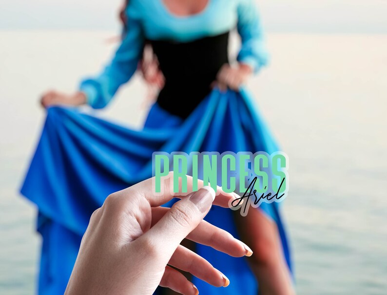 Op de afbeelding: Een transparante sticker met de woorden "PRINCESS Ariel" in groen en zwart. De sticker wordt vastgehouden voor een persoon die een blauwe jurk en een zwarte top draagt.
