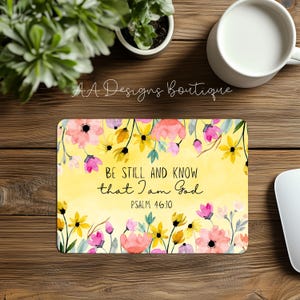 May include: A yellow background with a watercolor floral design. The text "Be still and know that I am God" is written in black cursive font. The text "Psalm 46:10" is written in black font below the cursive text.