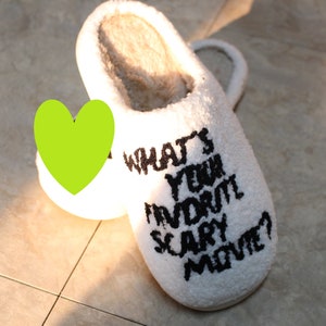 May include: White fuzzy slippers with black text that reads "What's your favorite scary movie?"