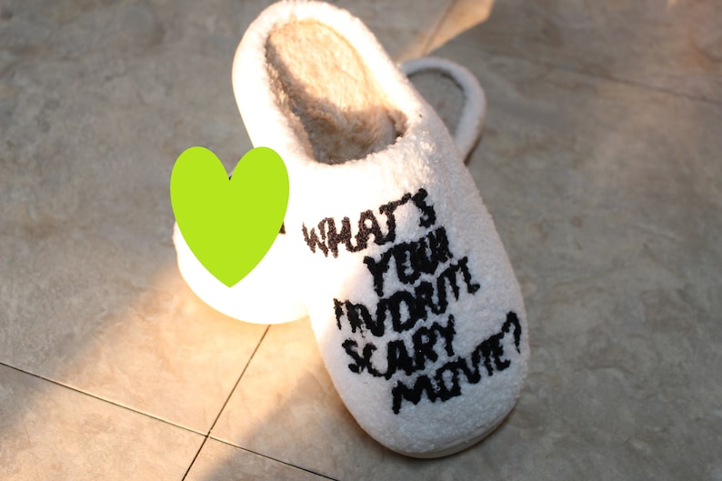 May include: White fuzzy slippers with black text that reads "What's your favorite scary movie?"