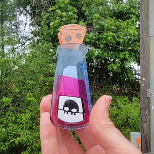Op de afbeelding: Een heldere, drankvormige fles met een kurken dop. De fles bevat een levendige roze vloeistof en heeft een wit etiket met een zwart schedelontwerp. De kurk is bruin met bruine vlekken.
