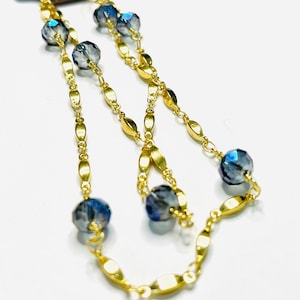 Può includere: Una collana a catena d'oro con maglie ovali e perline di cristallo blu.
