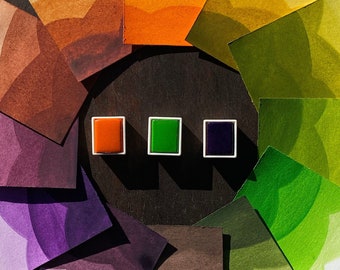 Könnte beinhalten: Ein Aquarell-Farbkreis mit Farbtönen von Orange, Gelb, Grün, Lila und Braun. Der Kreis besteht aus 10 einzelnen Karten, die in einem Kreis angeordnet sind. Drei kleine Farbtöpfchen sind in der Mitte des Kreises sichtbar, eines orange, eines grün und eines lila.