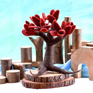 Puede incluir: Un árbol de fieltro con un tronco marrón y hojas rojas, de pie sobre dos rodajas de madera. El árbol es una pieza decorativa para una sala de juegos o una habitación infantil.