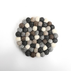 May include: A round, gray, brown, and white felt coaster made of small, round balls. The coaster is perfect for protecting surfaces from heat.