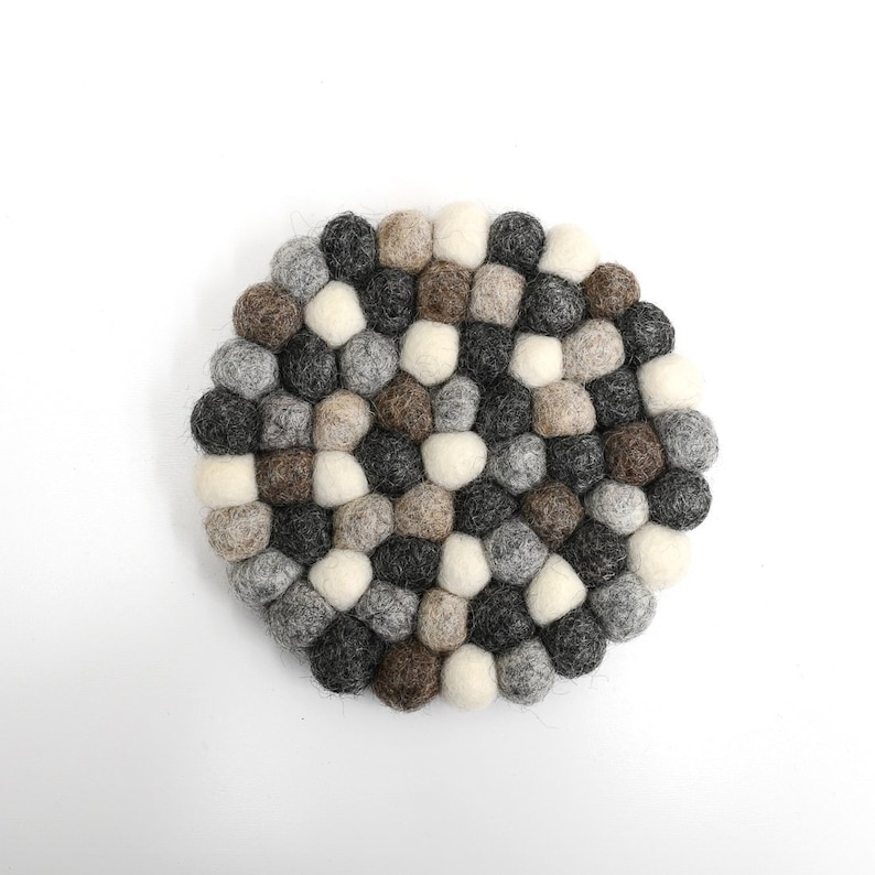 May include: A round, gray, brown, and white felt coaster made of small, round balls. The coaster is perfect for protecting surfaces from heat.