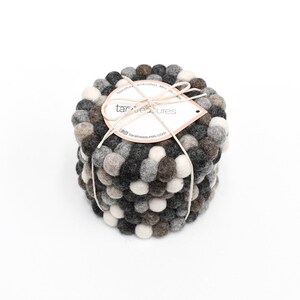 May include: Set of four gray, brown, and white felt coasters with a round shape. The coasters are made of small, round balls of felt. The coasters are stacked on top of each other. The coasters are tied together with a string and a tag that says "tara treasures".